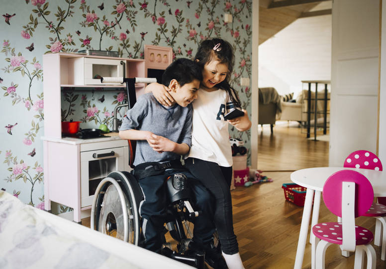 Together for Rights Young girl hugging a boy in a wheelchair, both looking at a mobile phone