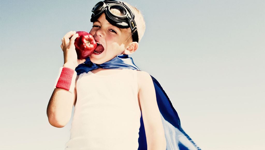 Young boy in superhero gear biting a red apple