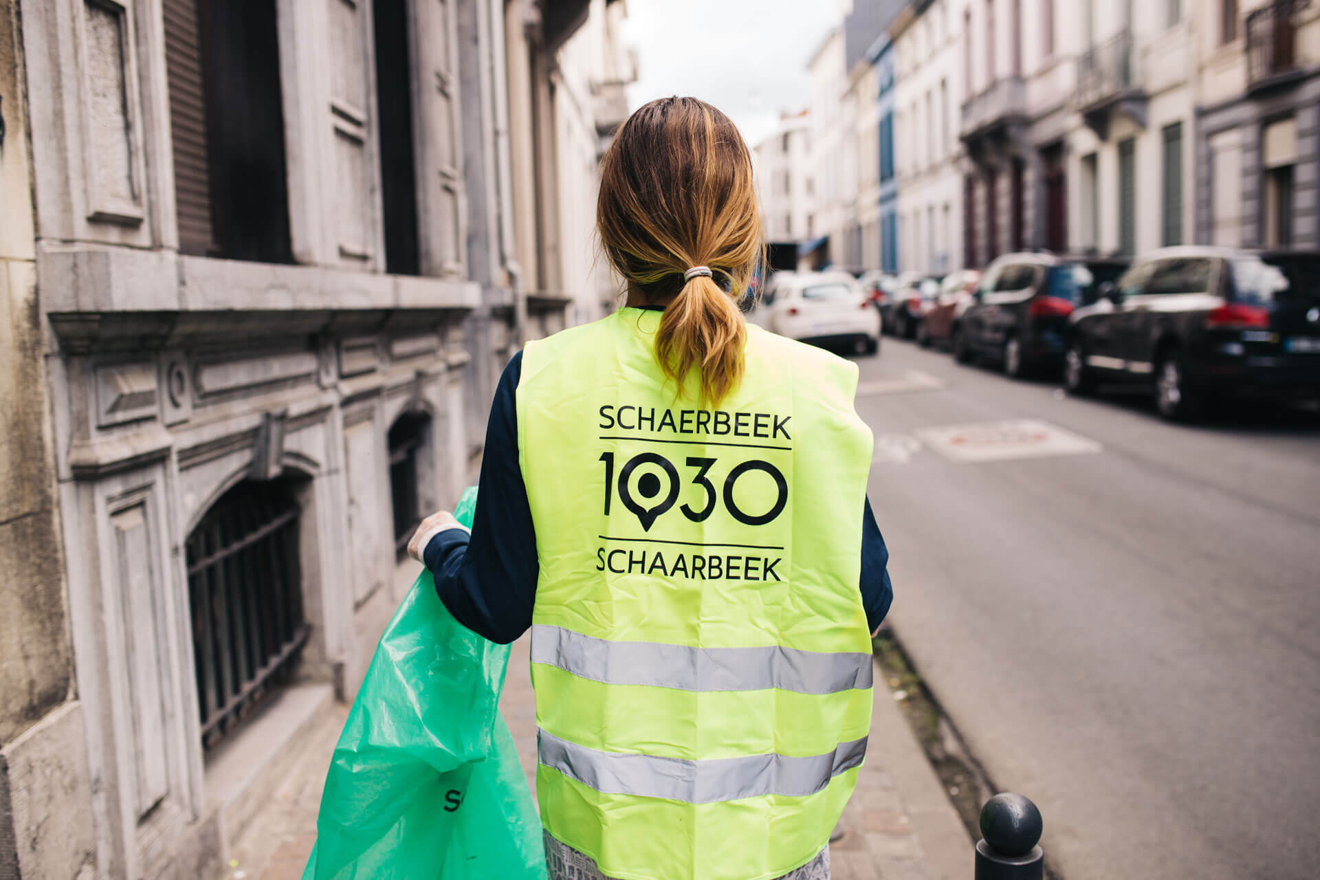 Person collecting rubbish on Schaerbeek streets wearing campaign jacket.