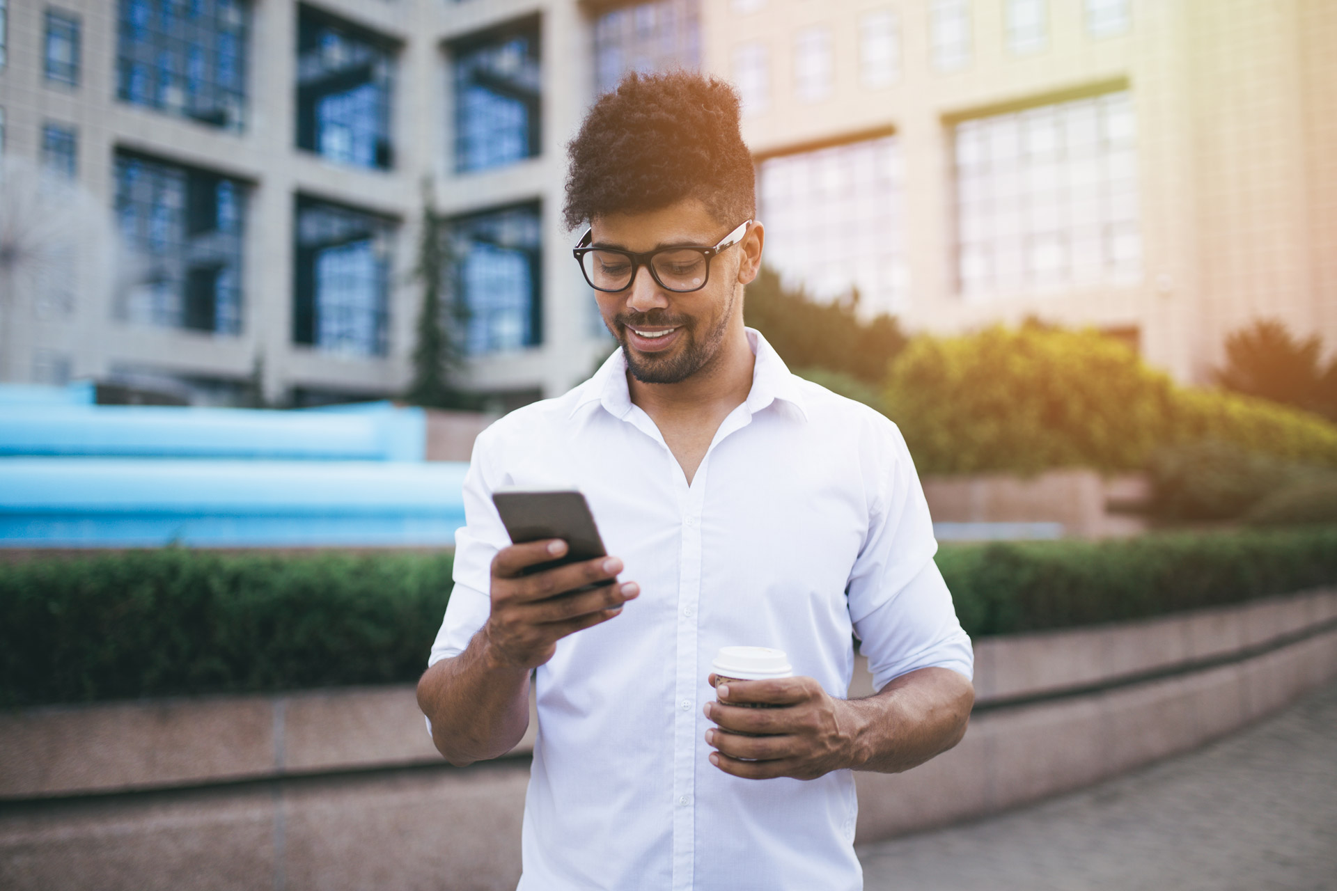 Young handsome Afro American man standing in front of huge modern business building smiling and talking on cell phone