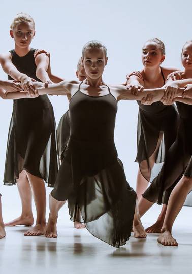 The group of modern ballet dancers dancing on gray studio background